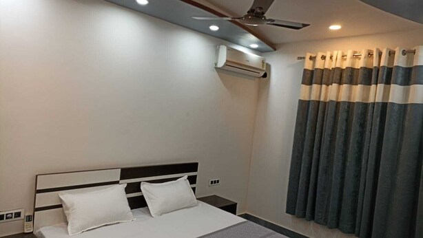 Ein Hotelzimmer mit Bett, Nachttisch, Deckenventilator, Klimaanlage und Vorhängen.