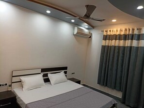A hotel room with a bed, a nightstand, a ceiling fan, an air conditioning unit, and curtains. - The Royal Scout Homestay (Barsar)