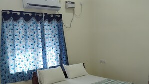A bedroom with a wooden bed, a window with blue floral curtains, an air conditioning unit, and a ceiling fan. - SANKARA RESIDENCY (Kanchipuram)