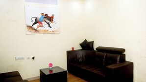 A living room with a brown leather sofa, a small black coffee table with a pink vase, and a painting of a bullfight on the wall. - SANKARA RESIDENCY (Kanchipuram)