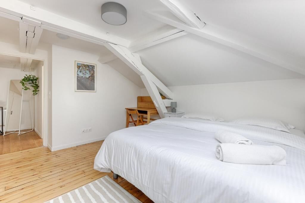 A bedroom with a sloped ceiling, a bed with white linens, a wooden desk, and a chair.