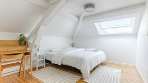 A bedroom with a sloped ceiling, a skylight, a bed, a desk, and a chair. - Le Magnolia - Proche de Disneyland (Lagny-sur-Marne)