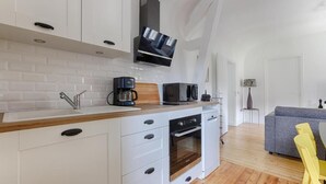 A modern kitchen with white cabinetry, a built-in oven, and a coffee maker. - Le Magnolia - Proche de Disneyland (Lagny-sur-Marne)