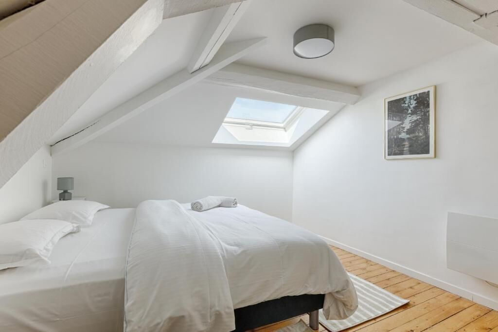 Un dormitorio con tragaluz, una cama, una mesita de noche y un cuadro enmarcado en la pared.