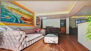 A living room with a large painting, a sofa, a chair, and a small table. - POM Holidays (Calangute)