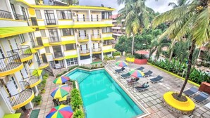 A multi-story hotel with balconies, a swimming pool, and outdoor seating with umbrellas. - POM Holidays (Calangute)
