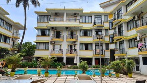 A multi-story hotel with balconies, a swimming pool, and lush greenery. - POM Holidays (Calangute)