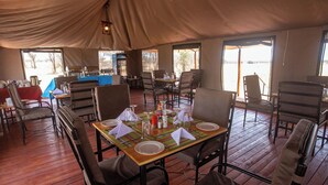 Un comedor con mesas dispuestas para cuatro, sillas y una estructura de techo cubierto.