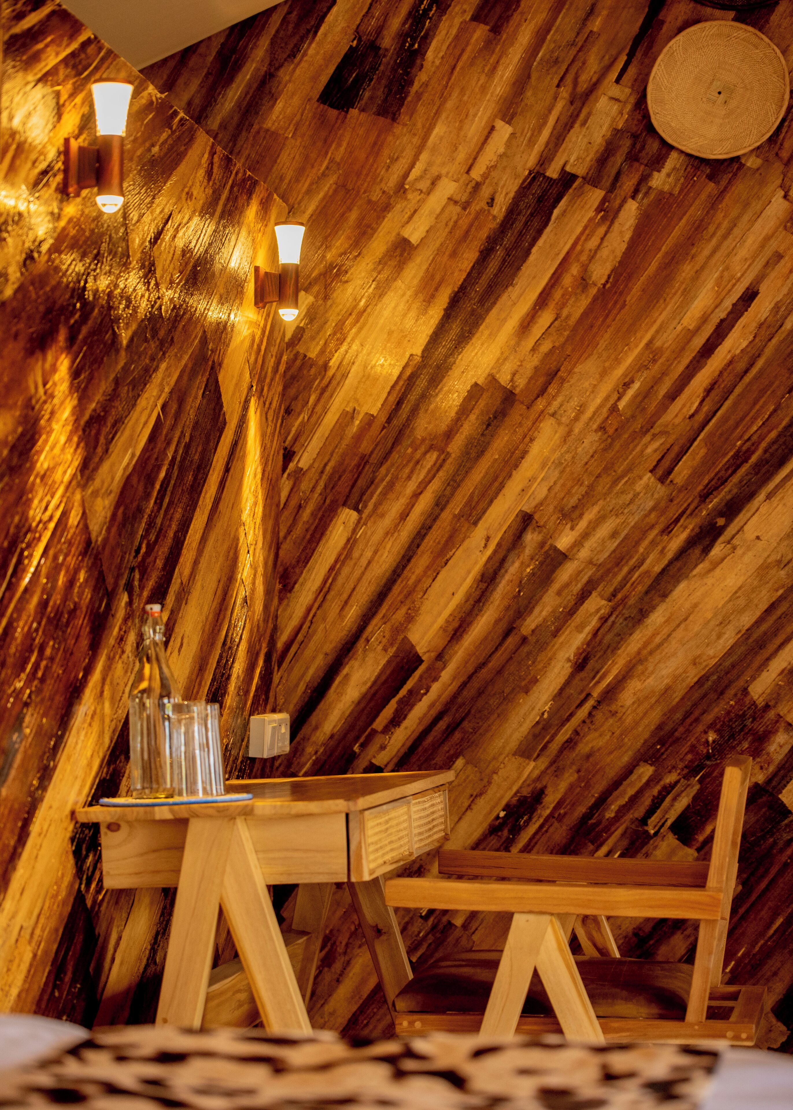 A wooden interior with a slanted ceiling, a table with chairs, and wall-mounted lights.