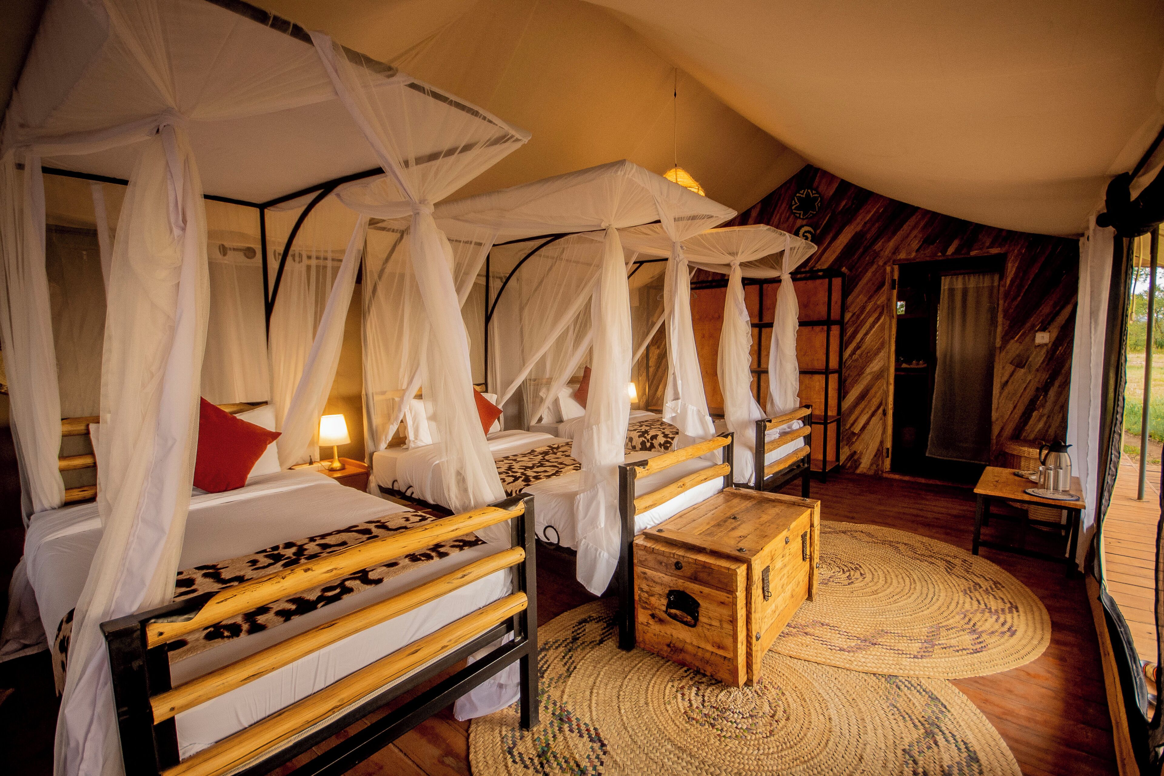 A room with four beds, each with a canopy, wooden headboards, and a woven rug.