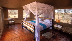 Una cama con dosel y cortinas, un escritorio de madera, una silla y una mesita de noche con lámpara en una habitación con techo cubierto.