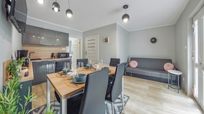 Una sala de estar moderna con un sofá, una mesa de comedor para cuatro personas y una zona de cocina con microondas y cafetera.