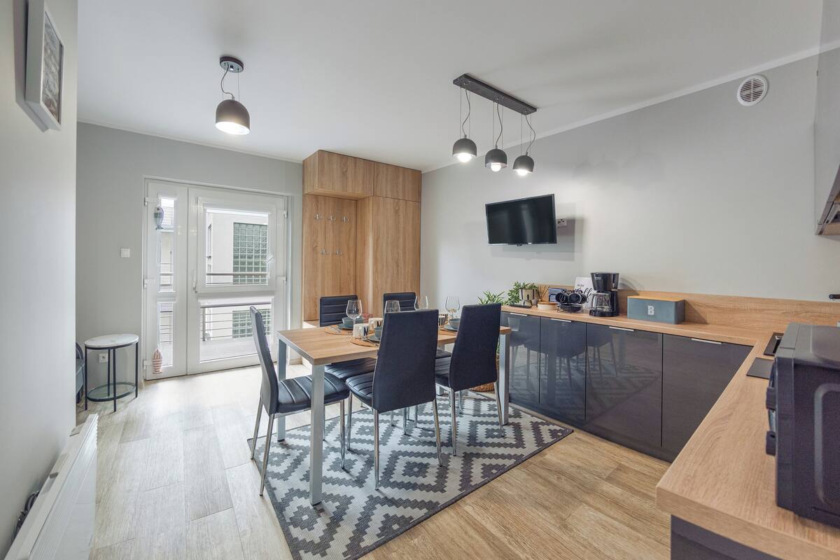 Eine moderne Küche mit Essbereich, Holzschränken, einem an der Wand befestigten Fernseher und einer Kaffeemaschine.
