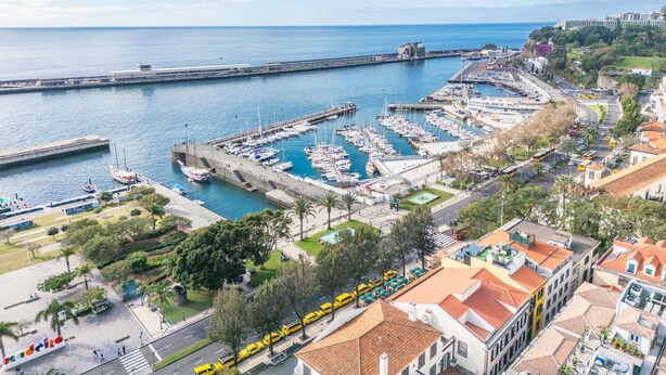 Un porto turistico con imbarcazioni ormeggiate, una passeggiata sul lungomare e edifici con tetti in tegole rosse.