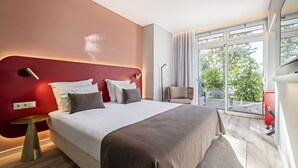 Una camera d'albergo moderna con un letto grande, una parete decorata in rosso, un balcone con vista e una scrivania con una sedia.