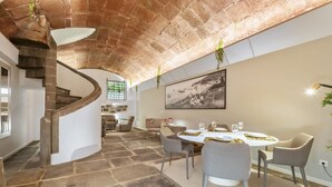Zona pranzo con tavolo rotondo, sedie grigie e una scala con parete in mattoni.