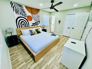 A bedroom with a bed, a desk, a ceiling fan, and a wardrobe.