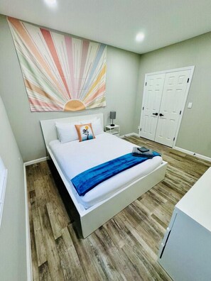 Quarto com cama, mesa de cabeceira, luminária, guarda-roupa e uma obra de arte na parede.