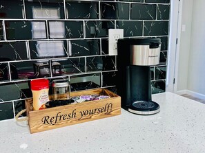 Uma bancada de cozinha com uma cafeteira, um recipiente para leite condensado e uma caixa de madeira com o texto 'Renove suas energias!'.