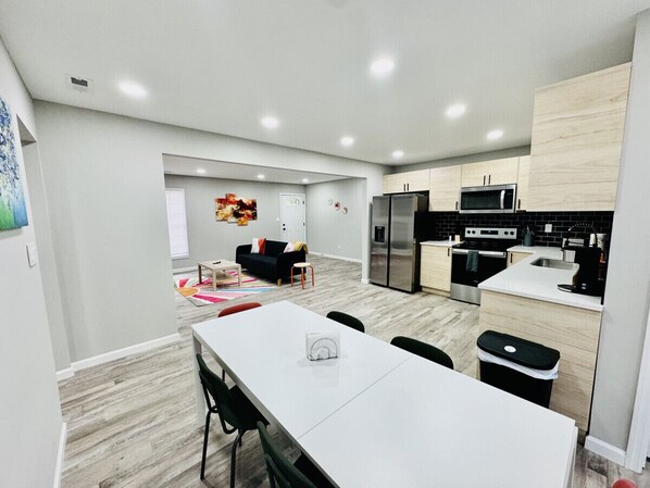 Una cocina moderna con comedor, que incluye una mesa blanca, sillas negras y un microondas.