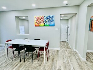Uma sala de reuniões moderna com uma mesa branca e cadeiras vermelhas, um quadro de uma árvore colorida na parede, e piso de madeira.