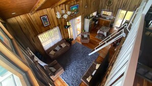 L’intérieur de ce chalet chaleureux comprend un espace de vie avec un canapé, une table basse et un tapis. On y trouve également une table à manger avec des chaises, un coin cuisine et un escalier menant à un étage supérieur.