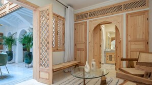 Ein geräumiges Zimmer mit einem Glastisch, Holzmöbeln und Blick ins Freie.