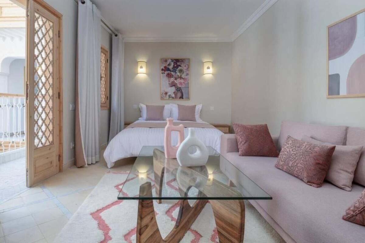 A bedroom with a bed, a glass coffee table, a sofa, and a painting on the wall.