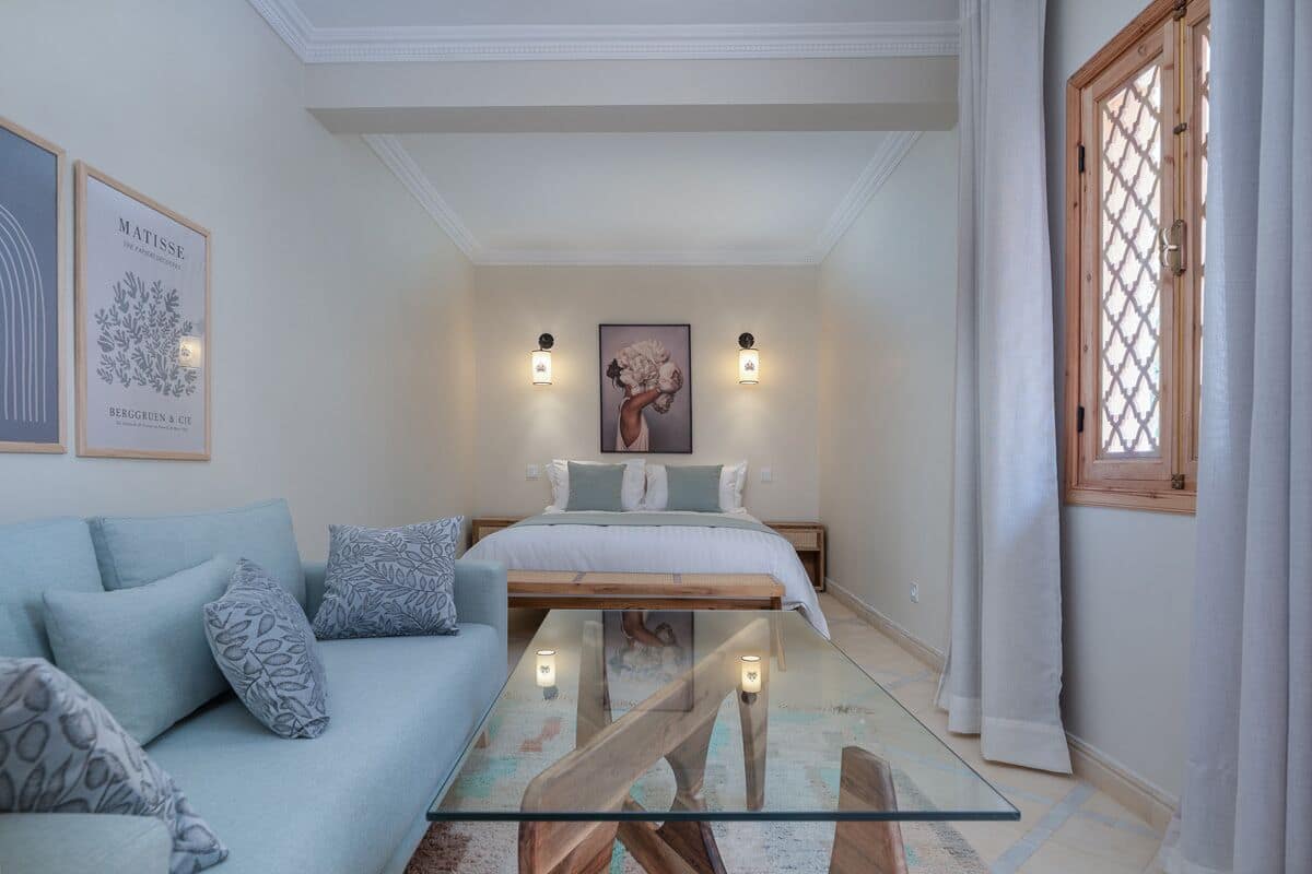 A bedroom with a bed, a glass coffee table, a sofa, and a painting on the wall.