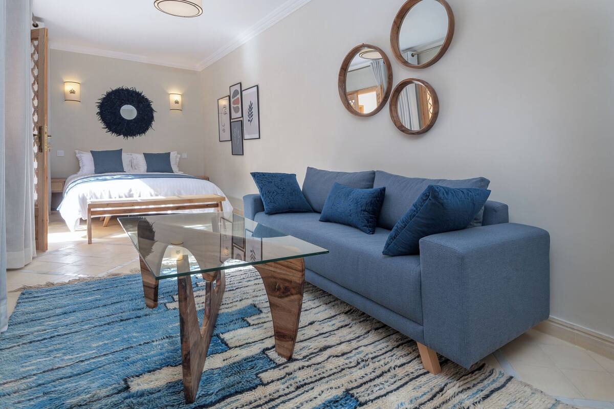 A modern bedroom with a bed, a glass-top coffee table, a blue sofa, and a blue shag rug.