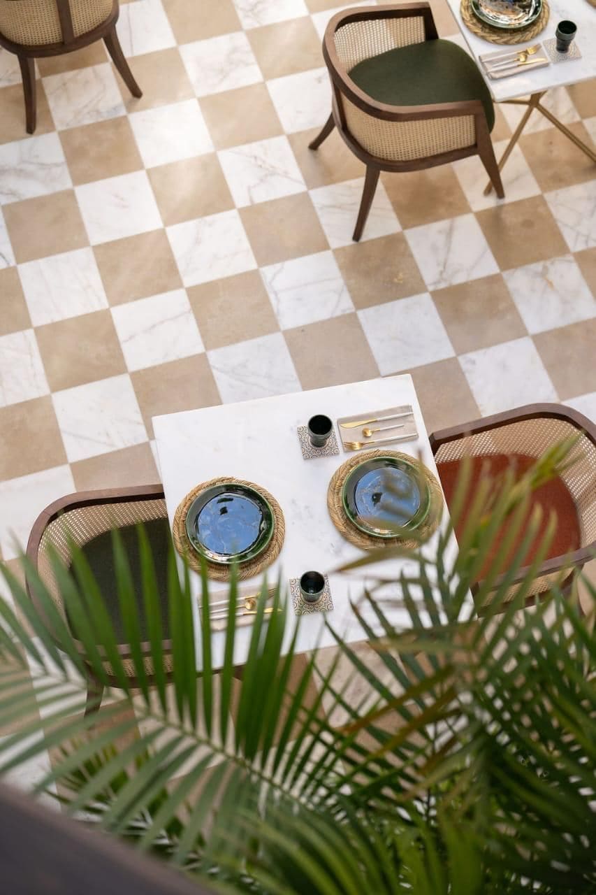 Un sol à carreaux, avec une table mise pour deux personnes, comprenant une assiette, des couverts et des verres.