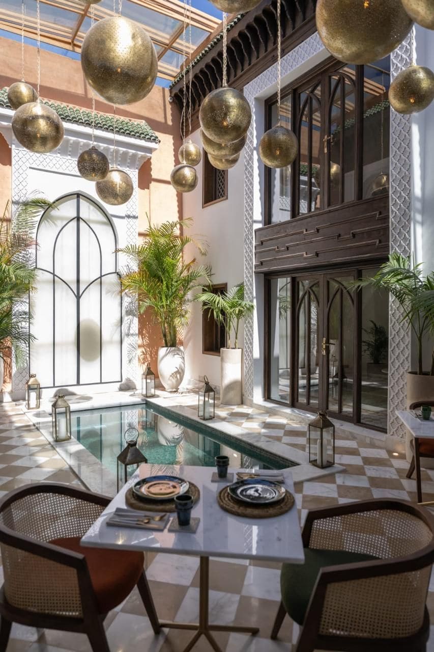 Un área junto a la piscina con suelo a cuadros, una mesa de comedor dispuesta con platos y cubiertos, y decoraciones esféricas colgantes.