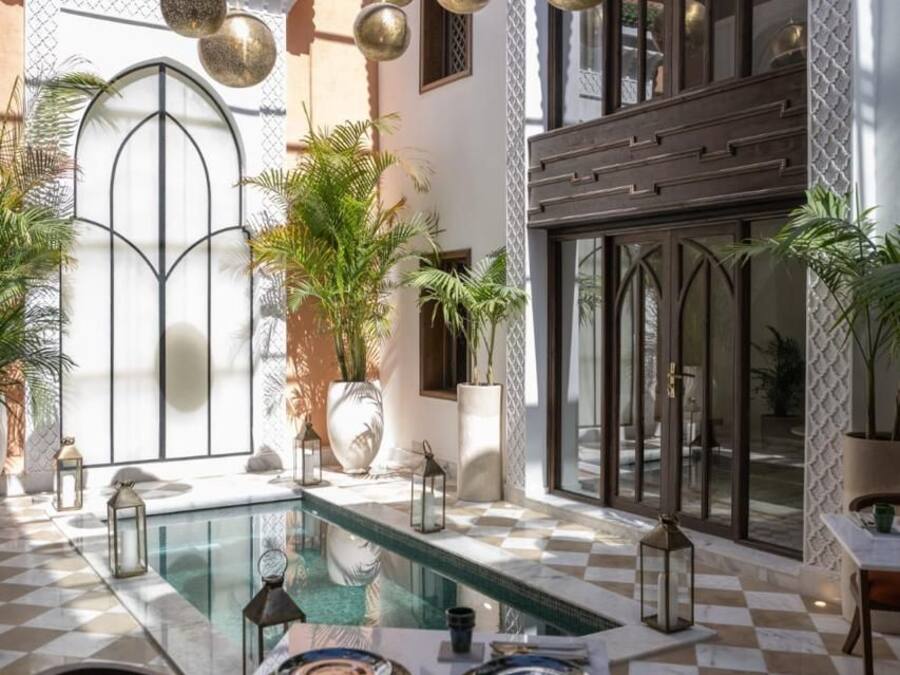 A poolside area with a checkered floor, a dining table set with plates and cutlery, and hanging spherical decorations.