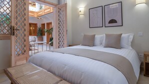 Ein Schlafzimmer mit einem großen Bett, einer hölzernen Sitzbank, einem Balkon mit Blick und zwei Wandleuchten.