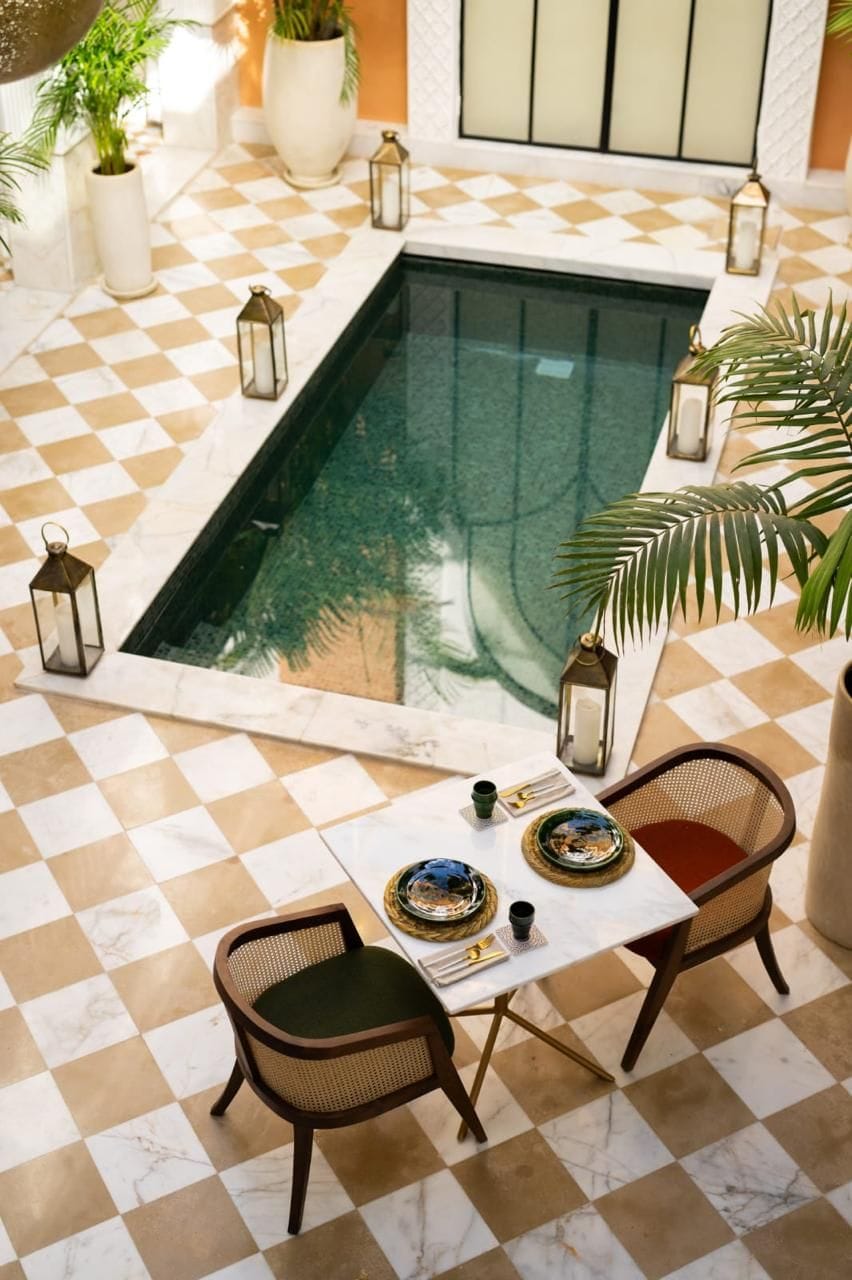 Un suelo a cuadros con una mesa de billar, dos sillas de mimbre y una mesa con platos decorativos y una vela.