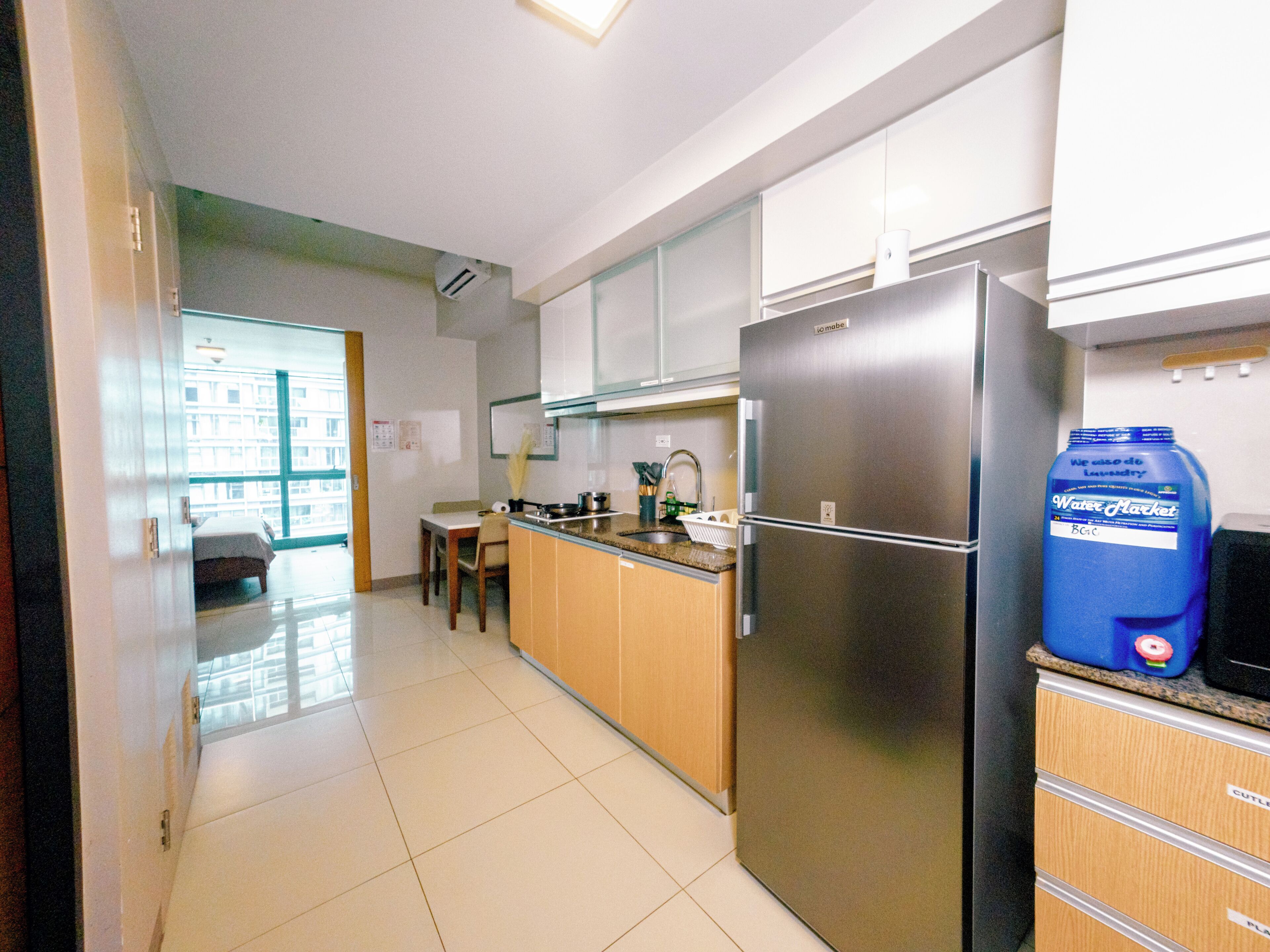 A modern kitchen with stainless steel appliances, wooden cabinets, and a large blue water jug on the counter.