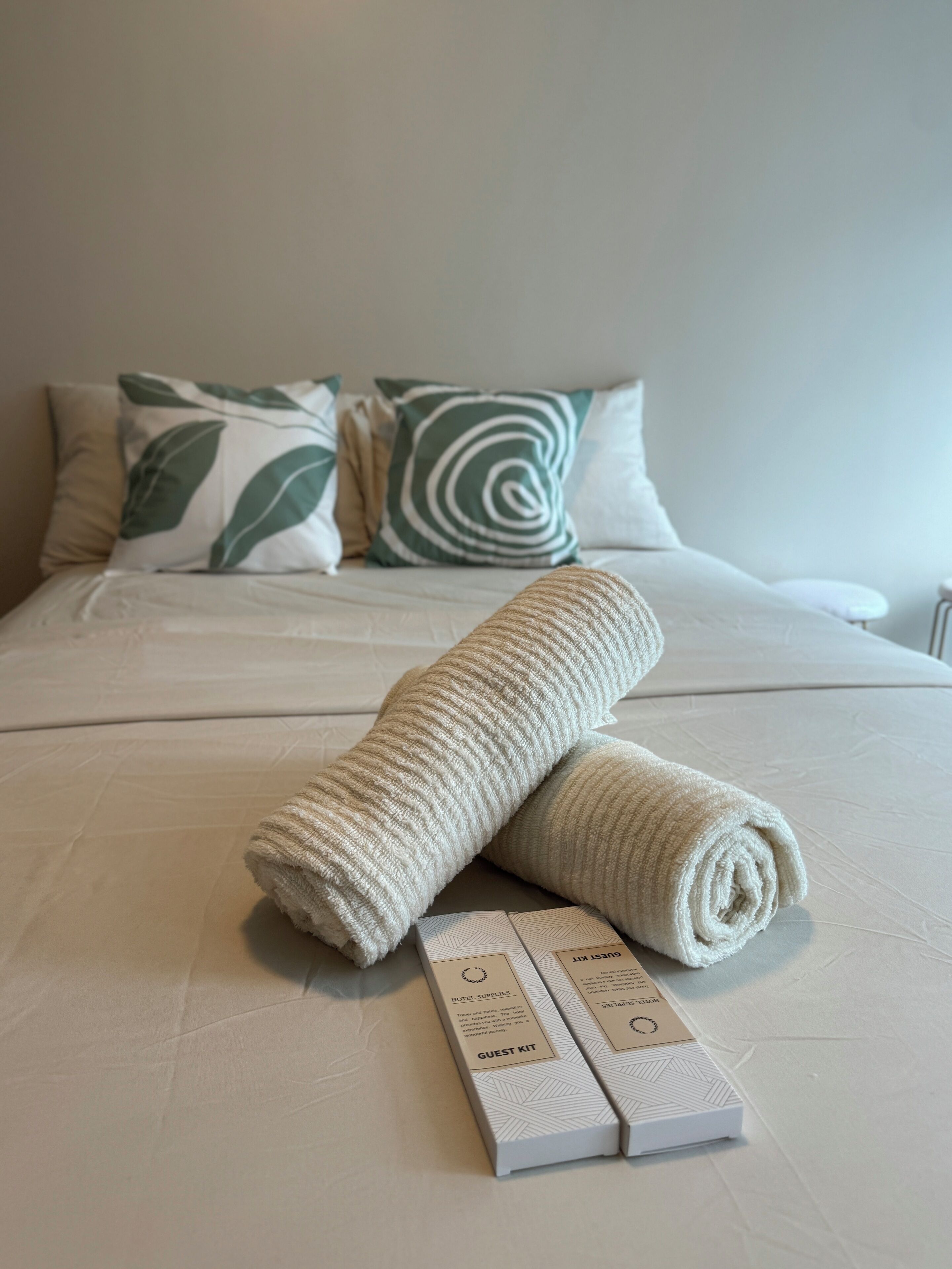 A neatly made bed with rolled towels and a guest kit on a white bedspread.