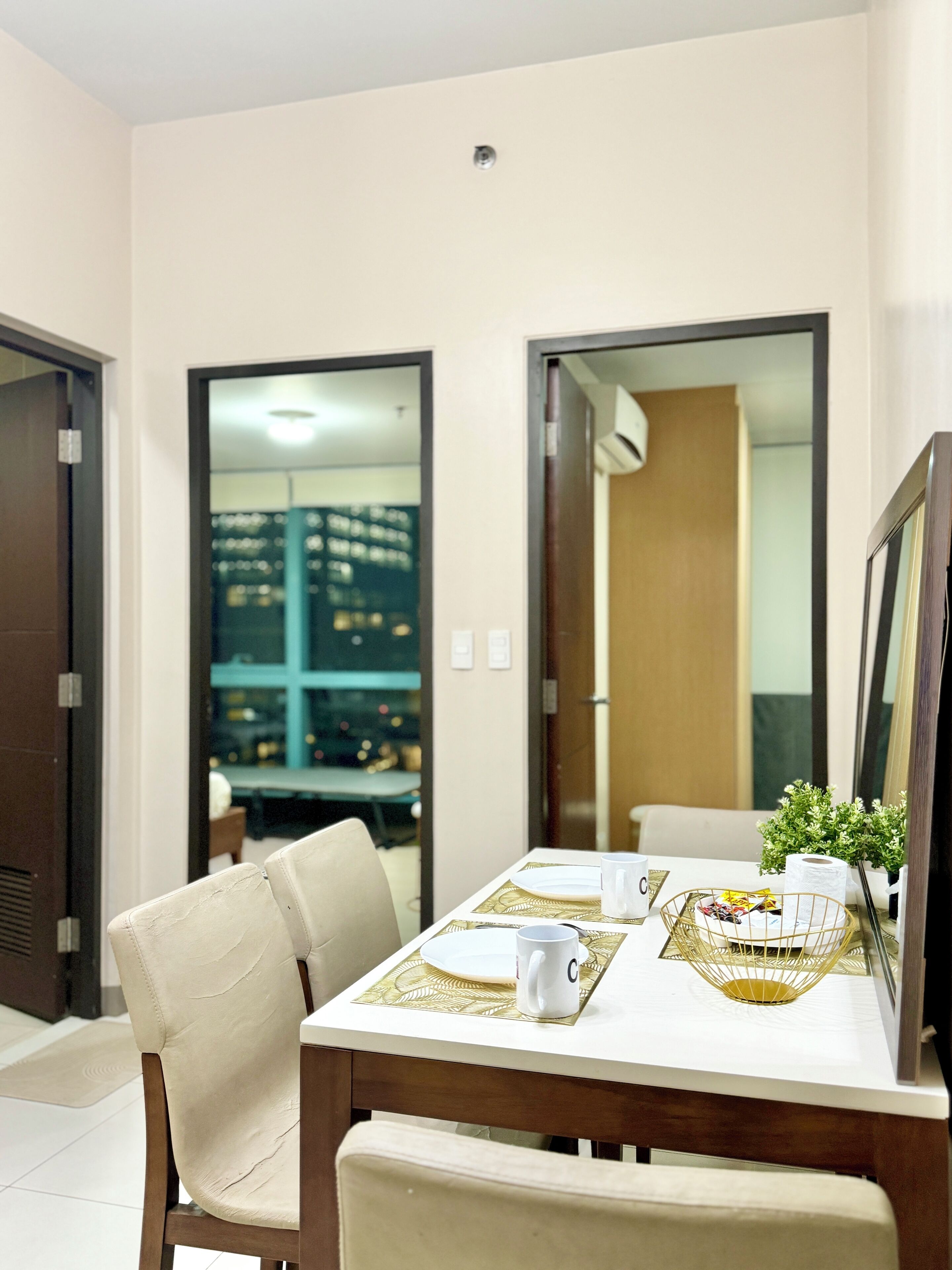 A dining area with a table set for two, chairs, a small plant, and a framed picture.