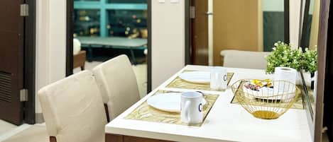 A dining area with a table set for two, chairs, a small plant, and a framed picture.