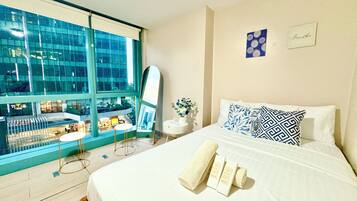 A hotel room with a large window, a bed with white linens, a mirror, and a small table with a vase of flowers.