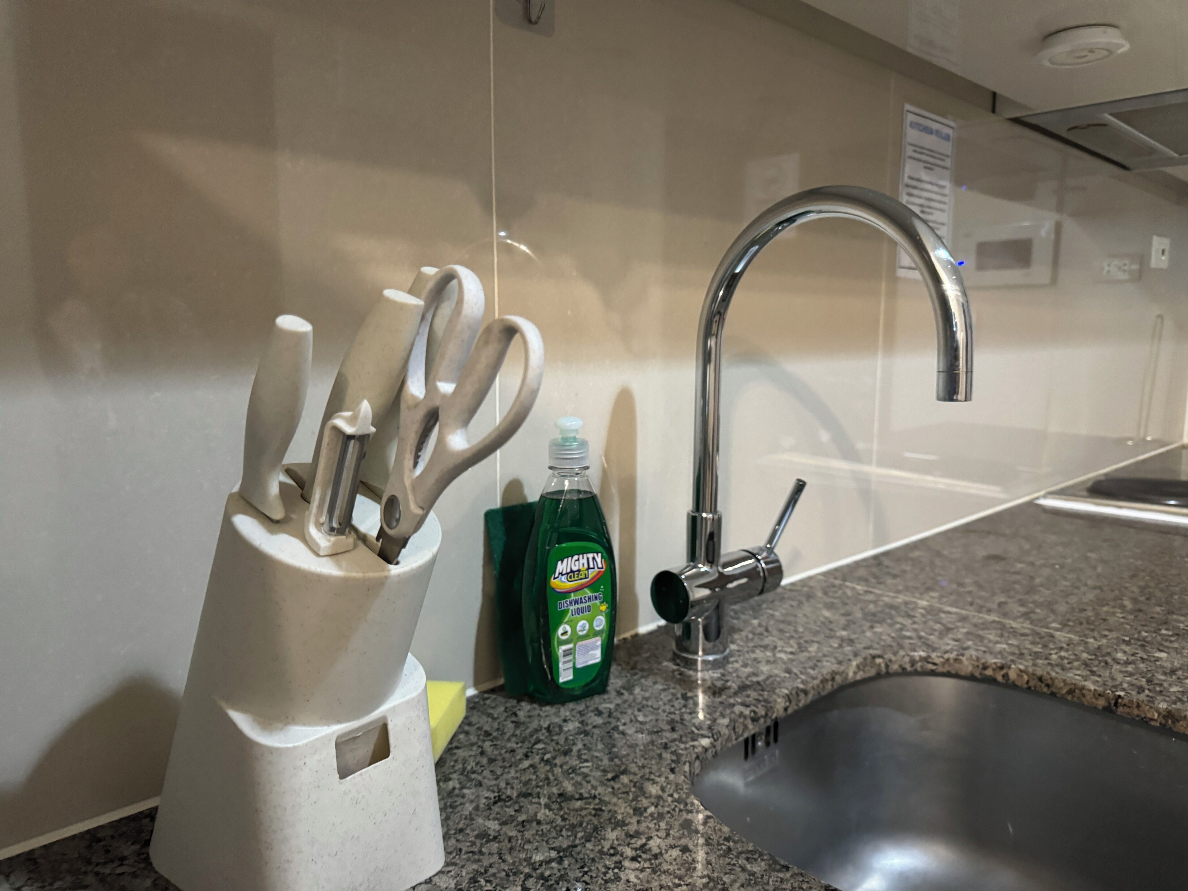 A kitchen sink with a faucet, a dish soap bottle, and a utensil holder with scissors and a knife.