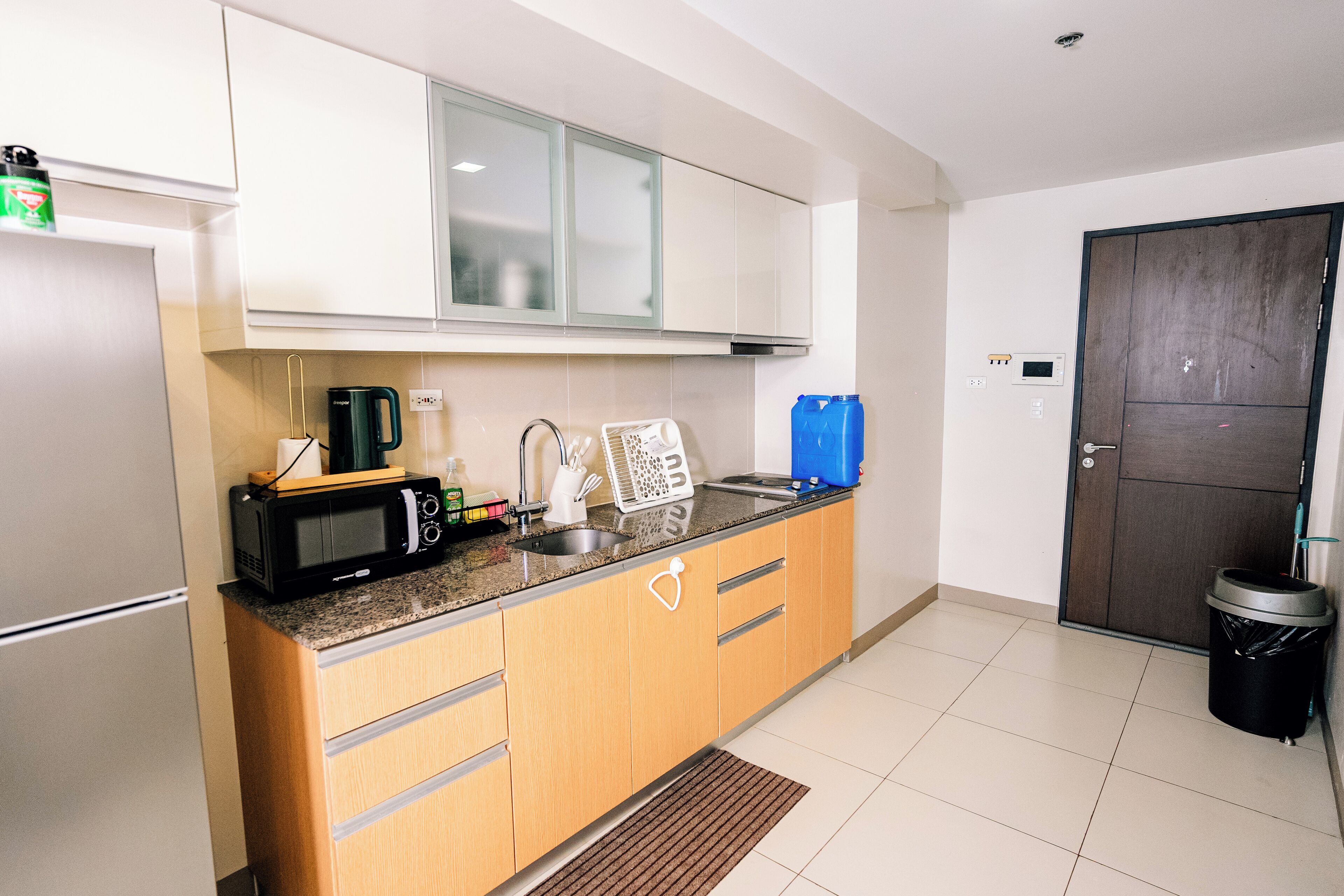 A compact kitchen with a microwave, kettle, and sink. There are cabinets above the counter and a door to the right.