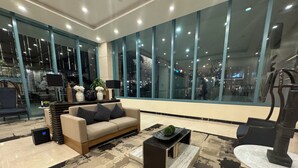 A modern interior with a beige sofa, a coffee table, and a large window offering a city view. - Cozi Uptown Executive Suite BGC (Taguig)