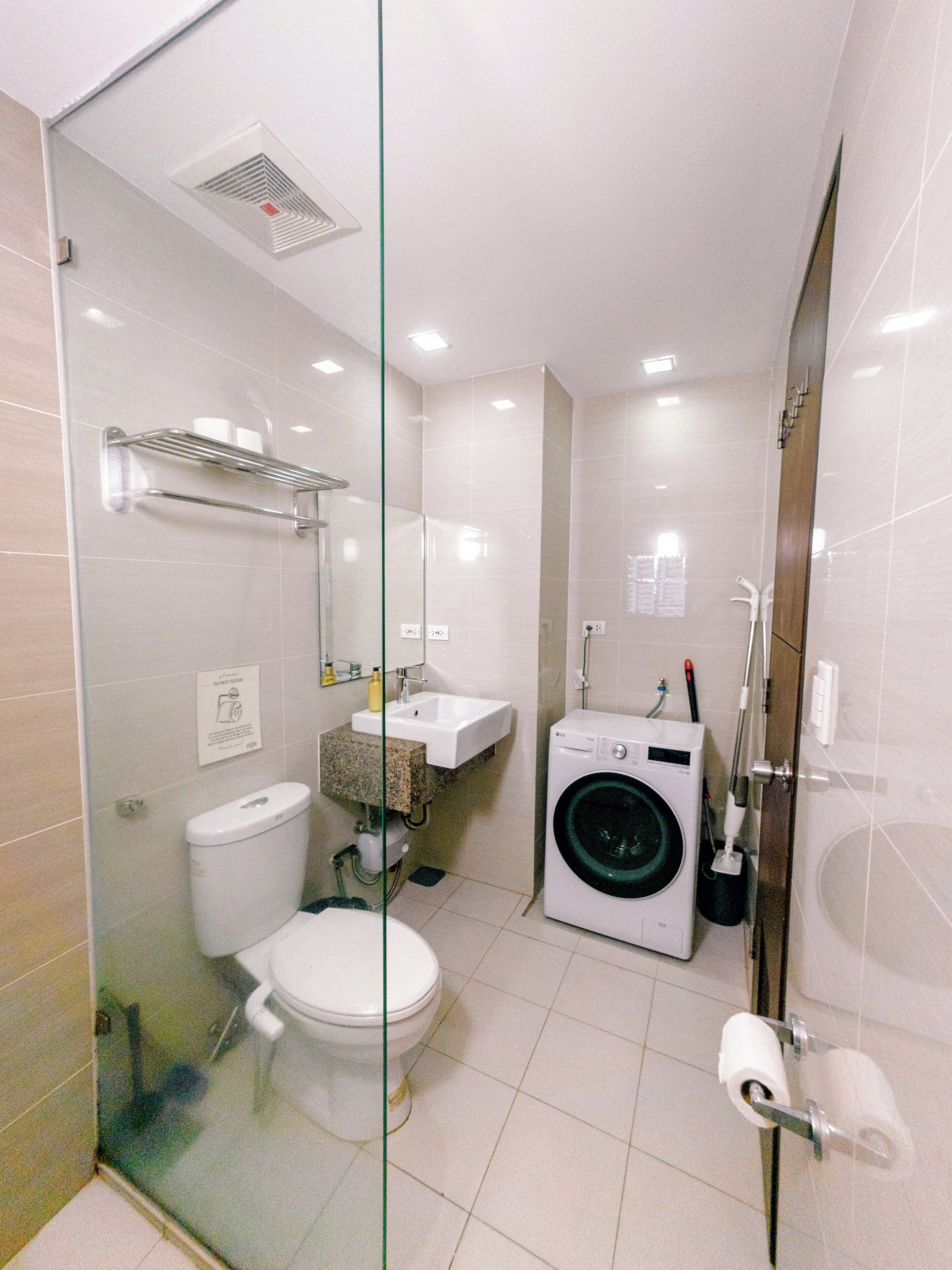 A compact bathroom with a toilet, sink, glass shower enclosure, and a washing machine.