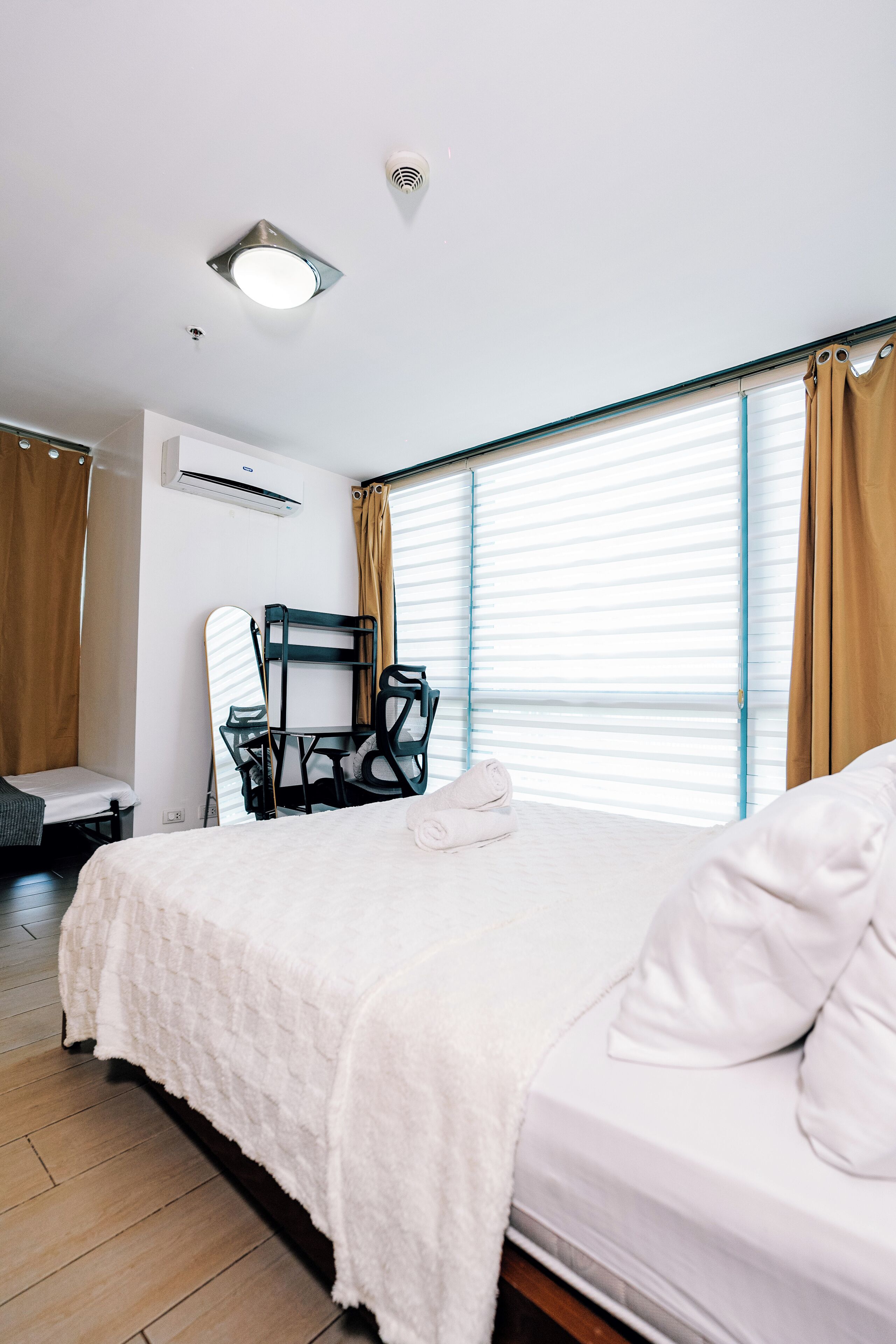 A hotel room with a bed, a chair, a desk, and a window with curtains.