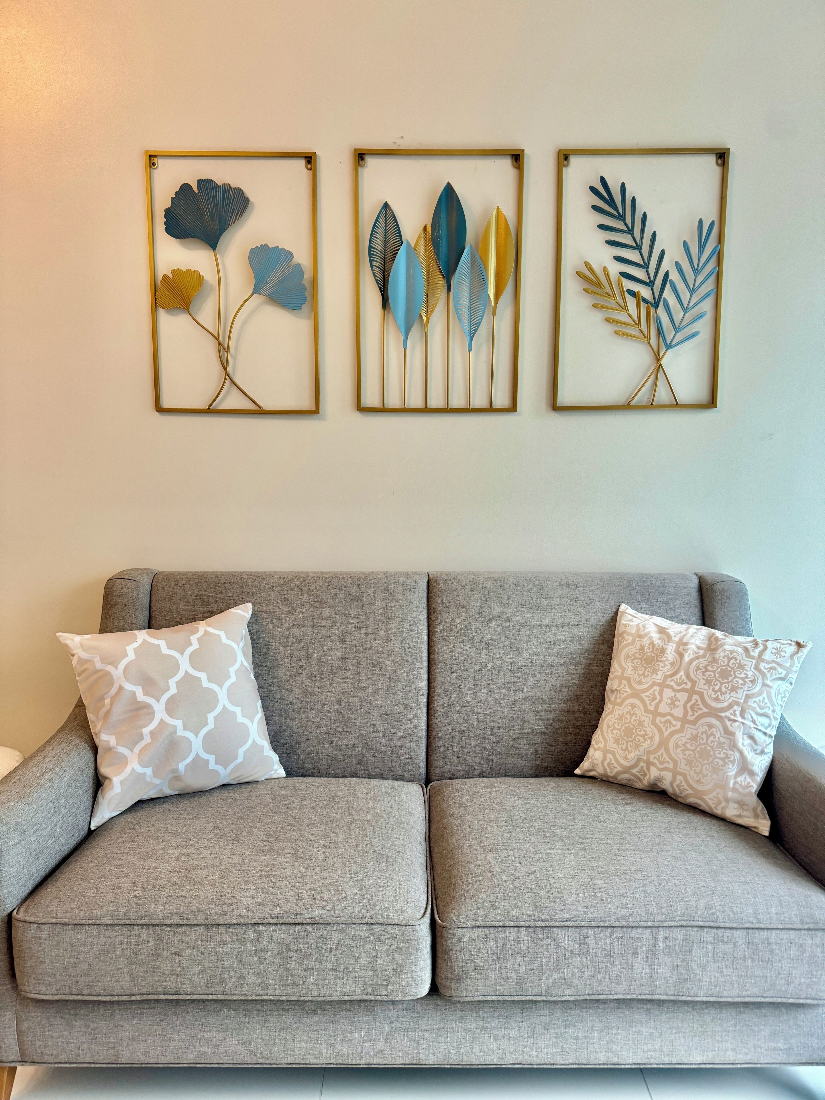 A grey sofa with two patterned pillows and three framed leaf artworks on the wall.