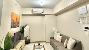 A modern living room with a flat-screen TV, a grey sofa, a coffee table, and a potted plant. - Cozi Uptown Executive Suite BGC (Taguig)
