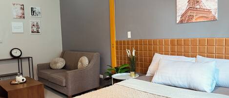 A hotel room with a bed, a sofa, a small table with a plant, and a wall clock.