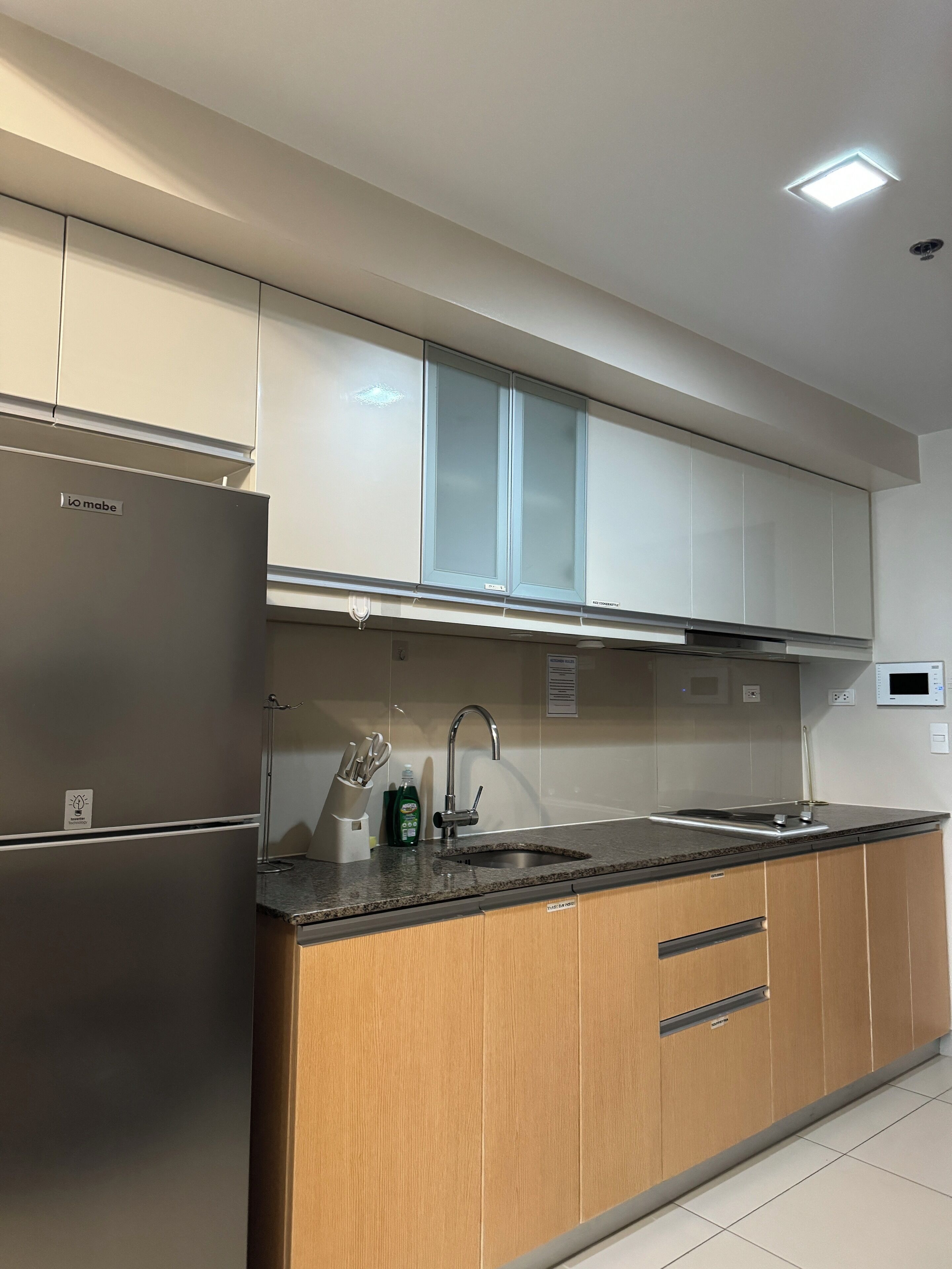 A modern kitchen with a stainless steel refrigerator, a double sink, and wooden cabinets.