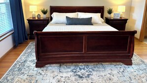 Un grand lit en bois sombre, surmonté d’une couvre-lit à motifs, et flanqué de deux tables de chevet ornées de lampes et de petits objets décoratifs.